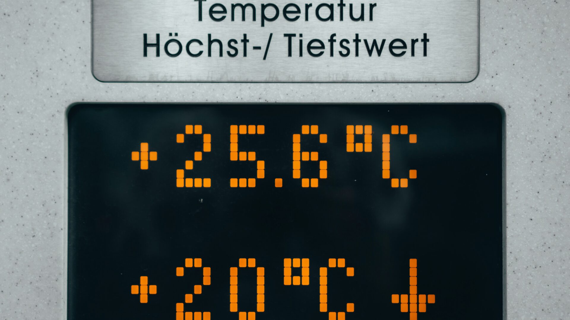 Digitale Anzeige mit der Beschriftung „Temperatur Höchst-/Tiefstwert“. Darunter leuchtet auf dem Display der Höchstwert mit +25,6 °C und der Tiefstwert mit +20 °C in orangefarbenen Pixelzahlen, begleitet von einem Abwärtspfeil.